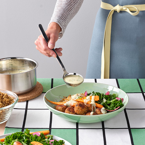 Una persona vierte una salsa cremosa en un tazón verde lleno de pescado, granos y verduras.