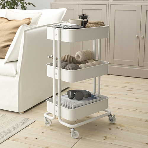 Carro de almacenamiento RÅSKOG blanco con estantes, ruedas, junto a la cama.