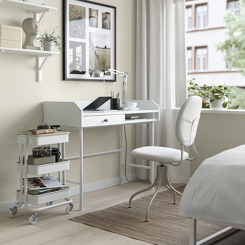 Configuración de la oficina en casa: carro RÅSKOG blanco debajo del escritorio con artículos, computadora portátil y suministros en el escritorio, silla blanca con patas de metal.
