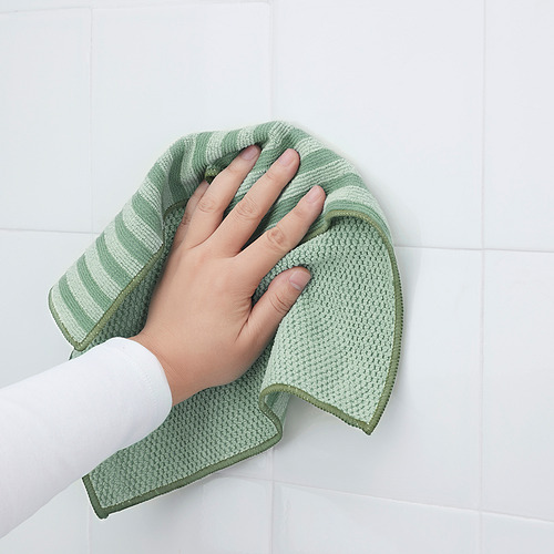 Persona sosteniendo un paño de microfibra verde, lado suave para una limpieza suave, lado grueso para manchas difíciles.