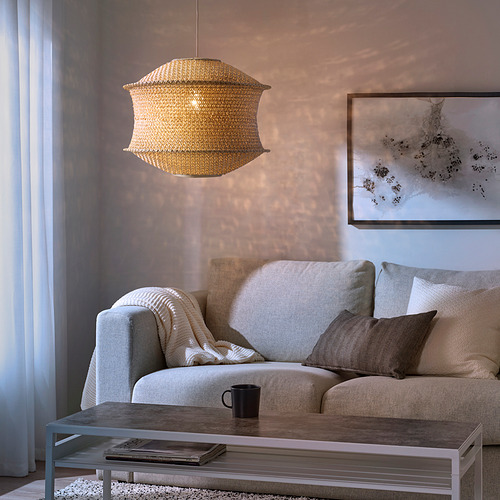 Colgante BLÅSTÅNG dorado sobre sofá gris, fundición de patrones de pared, con mesa de centro, libro y taza.