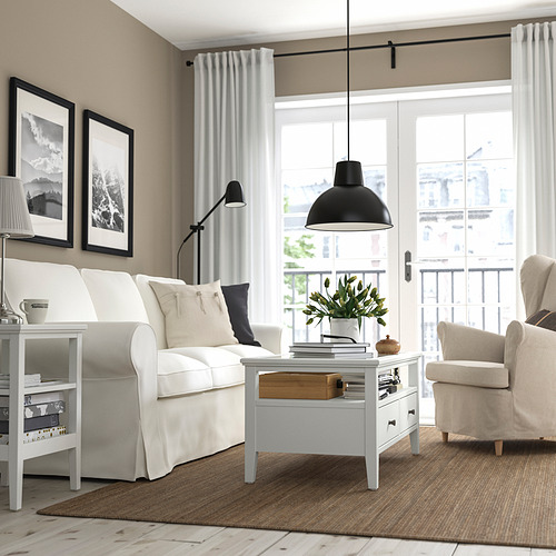 Moderno salón con mesa de centro, sofá, sillón y grandes ventanales de IDANÄS. La decoración incluye fotos, lámpara y alfombra.