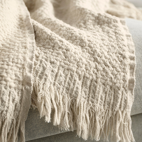 Manta texturizada de color blanco roto con bordes con flecos, que muestra la calidad tejida a mano y la tela natural.
