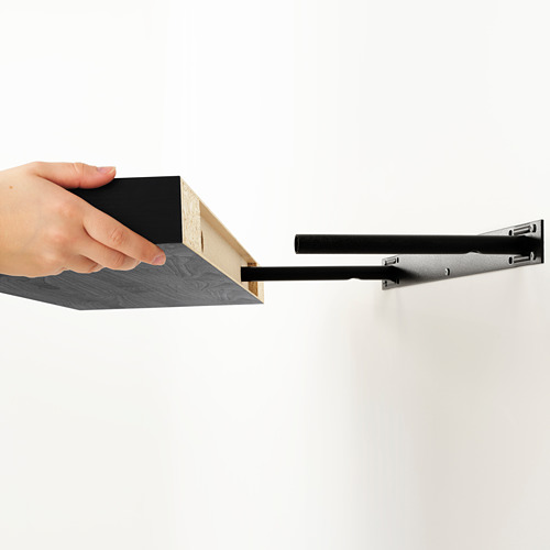 Una mano que sostiene una moderna estantería de madera, mostrando sus discretos soportes colgantes, casi invisibles, que se funden con la pared.