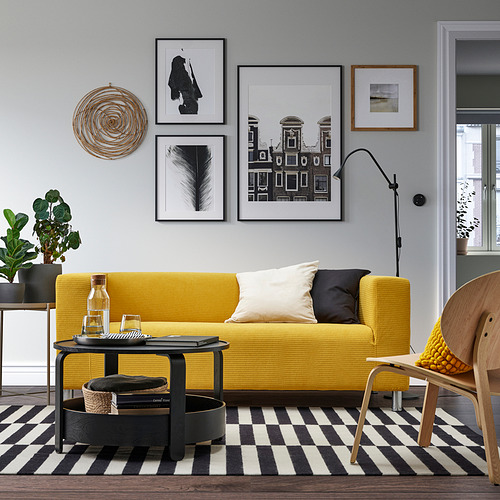 Sala de estar moderna con sofá amarillo, alfombra blanca y negra, mesa de almacenamiento BORGEBY y arte de pared.