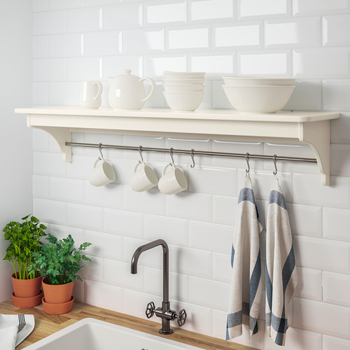 Un estante blanco de la cocina sostiene vajilla blanca sobre tazas y toallas a rayas, montadas en una pared de azulejos.