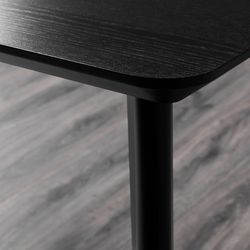 Primer plano del elegante borde de las mesas LISABO negras, con un acabado de madera lisa y una robusta pata de metal.