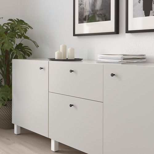 Mueble blanco con pomos negros; La parte superior sostiene velas, la parte inferior tiene cajones, contra la pared con arte enmarcado.