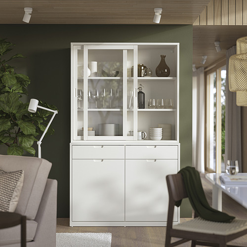 Aparador TONSTAD blanco con puertas de cristal para exhibir platos y vasos. Puertas correderas, estantes móviles, pared verde, sillas de madera.