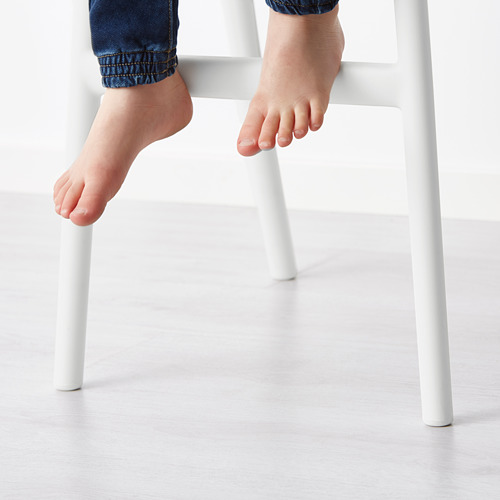 Pies de niño en silla junior blanca. Altura perfecta para la mesa de comedor, proporcionando un cómodo apoyo para los pies.