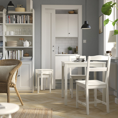 Pequeña mesa de comedor y juego de sillas de madera blanca. Diseño limpio y moderno. Forma parte de la serie HAUGA. Paredes de color gris claro y suelo de madera natural.