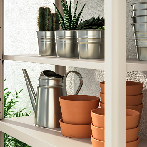 Estantería blanca con macetas de terracota, regaderas metálicas y pequeños cactus en macetas. Ideal para el almacenamiento y la organización de plantas en interiores o exteriores.