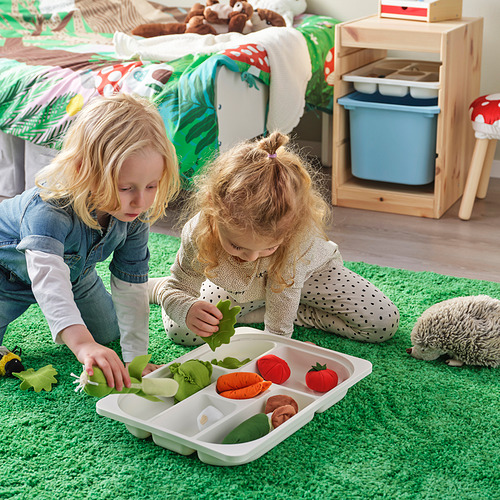 Dos niños juegan con juguetes de fantasía, organizando frutas y verduras en una bandeja TROFAST sobre una alfombra verde.