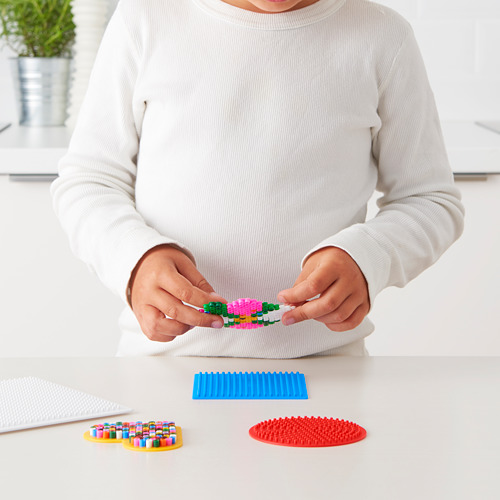 Un niño ensambla cuentas de colores sobre una base azul. Representa el juego de cuentas PYSSLA, que promueve la creatividad y el desarrollo de habilidades motoras.