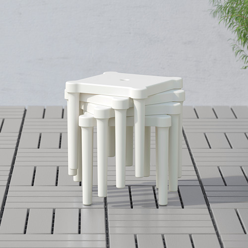 Taburetes infantiles blancos apilables al aire libre en patio embaldosado, ideales para jugar y hacer manualidades.