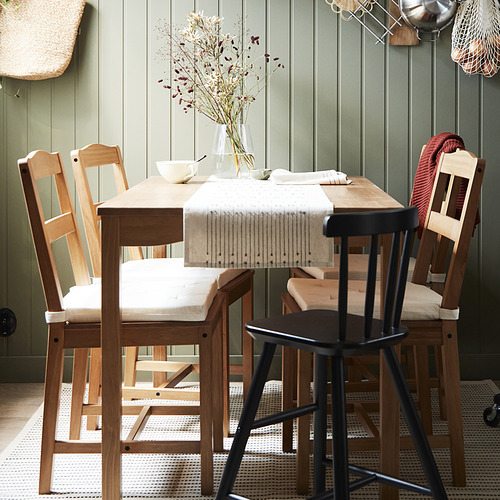 Mesa de comedor de madera rústica con sillas, paredes verdes, cojines, corredor de tela, flores secas.
