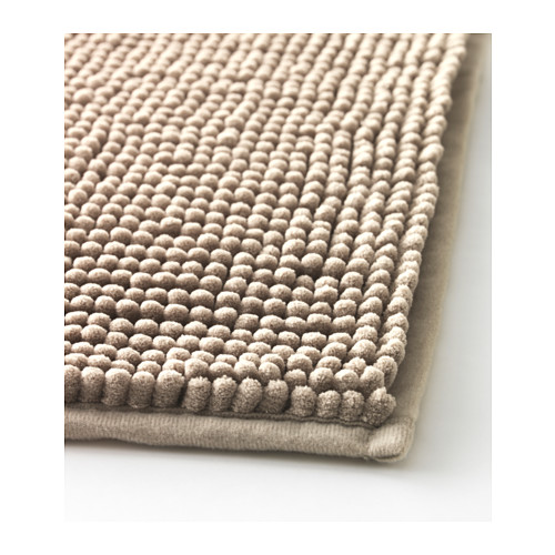 Primer plano de una alfombra de baño beige de felpa con una superficie suave y texturizada y un borde plano.
