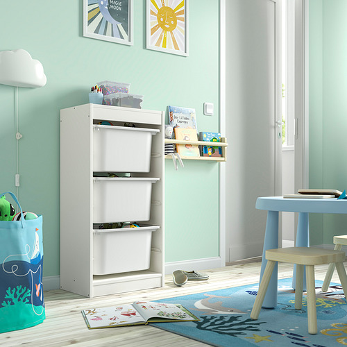 Habitación para niños con almacenamiento TROFAST blanco, juguetes, libros y una mesa azul junto a la ventana.
