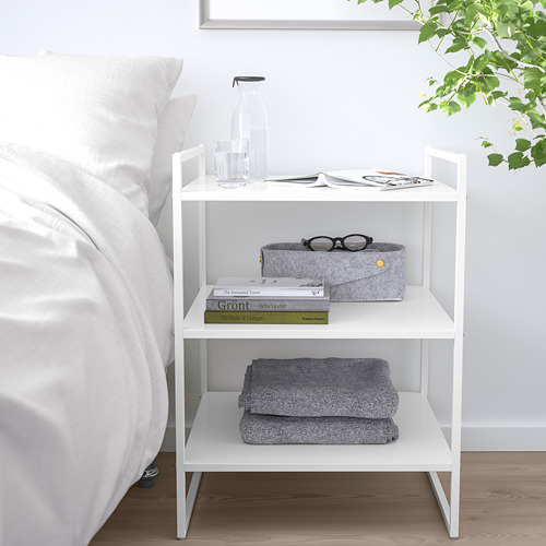 El mueble de almacenamiento blanco JONAXEL, de acero con recubrimiento en polvo, cabe perfectamente junto a una cama, más pequeño que la cama, contiene ropa doblada, libros y artículos de decoración.