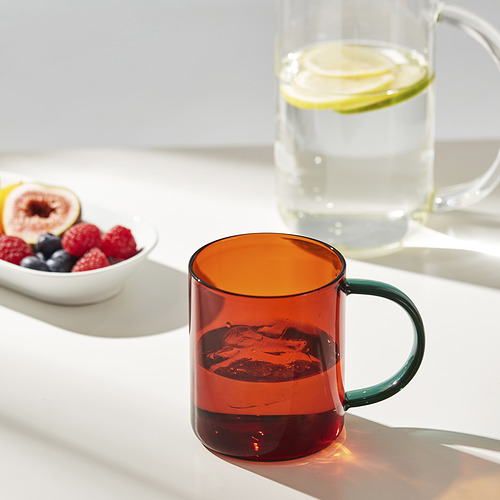 Taza de vidrio colorida con asa en la mesa cerca del tazón de fruta.