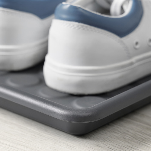 Primer plano de una zapatilla blanca y azul que descansa sobre una alfombrilla de plástico gris sobre un suelo de madera.