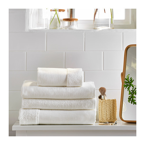 Estante de baño limpio y minimalista con toallas blancas SALVIKEN, cuidadosamente dobladas, junto a una cesta tejida, una planta y un espejo.