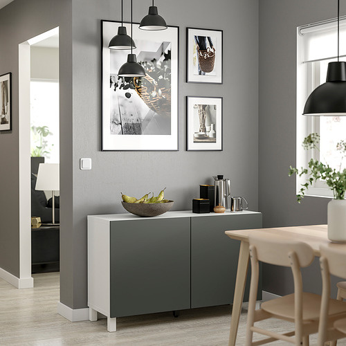 Sala de estar moderna con unidad de almacenamiento BESTÅ gris, encimera blanca, con luces colgantes negras, fotos enmarcadas y sillas de madera.