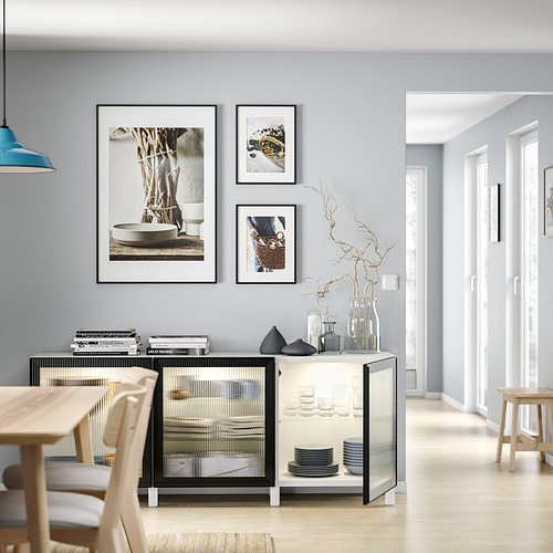 Sala de estar moderna con paredes de color gris claro, suelo de madera y zona de comedor. Muebles en blanco y negro, obras de arte enmarcadas, jarrones y libros.