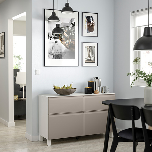 Modern dining area with light gray BESTÅ sideboard, black chairs, and pendant lamps. Artwork and fruit bowl on the sideboard.