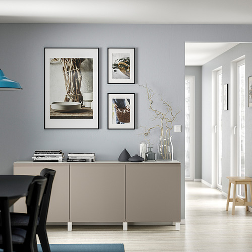 Sala de estar moderna con aparador BESTÅ, sillas negras, lámpara azul, cuadros enmarcados y jarrones.