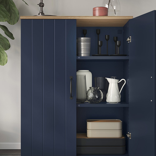 Mueble azul marino con tapa de roble, donde se exhiben jarrones, candelabros y cajas. Panel superior fijado a la pared.
