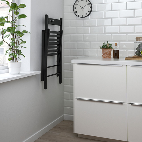 Cocina con gabinetes blancos y placa para salpicaduras, silla colgante negra estilo escalera, plantas y reloj.