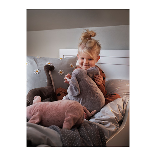 Niña abraza un elefante de peluche gris de juguete en la cama con almohadas de margaritas blancas. Acogedor y cálido.