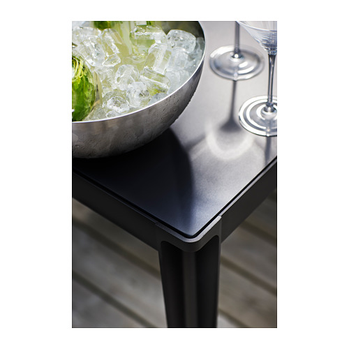Imagina una mesa de exterior con un cuenco metálico y vasos. El cuenco contiene hielo y limas. La mesa tiene una tapa oscura y patas metálicas.