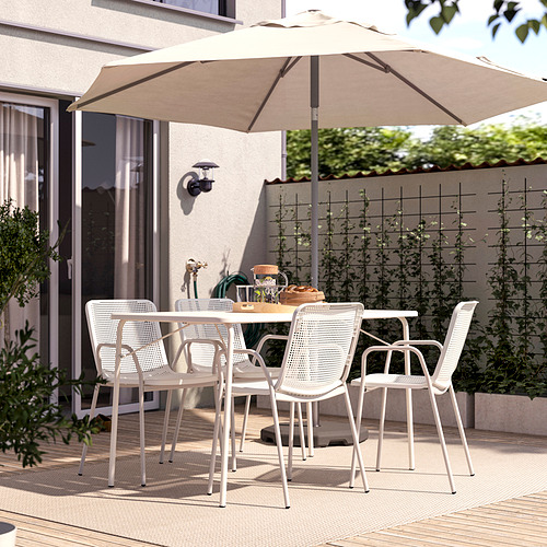 Moderno patio exterior con mesa y sillas blancas TORPARÖ, sombrilla beige, situado en una cubierta de madera, rodeado de vegetación.