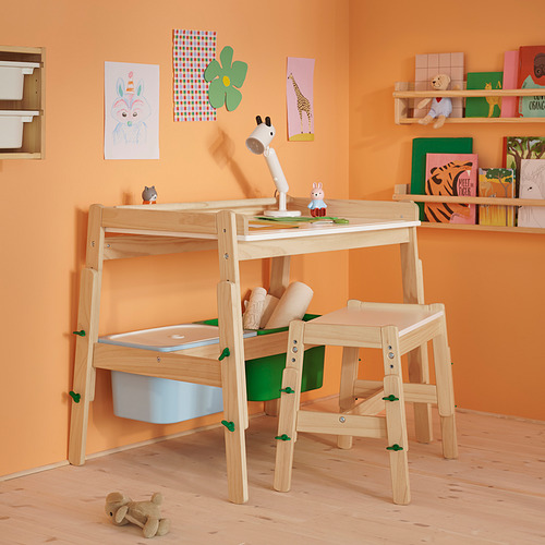 Habitación infantil con escritorio y silla de madera FLISAT . El escritorio tiene almacenamiento, una lámpara y suministros de arte. La silla tiene altura ajustable. Los estantes contienen libros y juguetes.