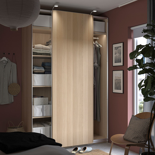 Dormitorio moderno con armario PAX, luces incorporadas, ropa organizada, pared a rayas, mesita y planta.