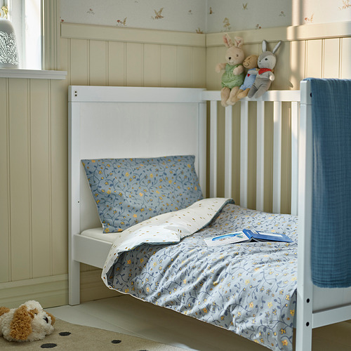Cama para niños debajo de la ventana, edredón floral azul, animales de peluche.