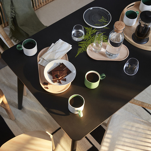 Comedor moderno con mesa LISABO negra, tazas, vasos, plantas y chocolates.