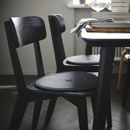 Dos sillas LISABO de madera negra cerca de una mesa apilada y platos. Construcción robusta, diseño simple.