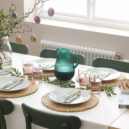 Un juego de mesa de comedor con vasos IKEA 365+, jarra verde, platos, cubiertos y servilletas, listo para una comida.