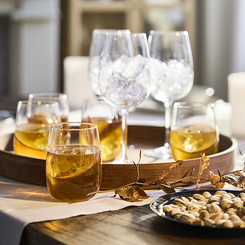 Cuatro copas de vino de diferentes estilos en una bandeja de madera con pistachos y hojas secas. Vasos y bandeja sobre una mesa de madera con un mantel color crema.
