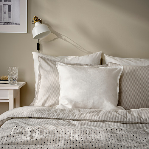 Dormitorio de tonos neutros con ropa de cama a rayas, mesita auxiliar blanca y lámpara de pared.