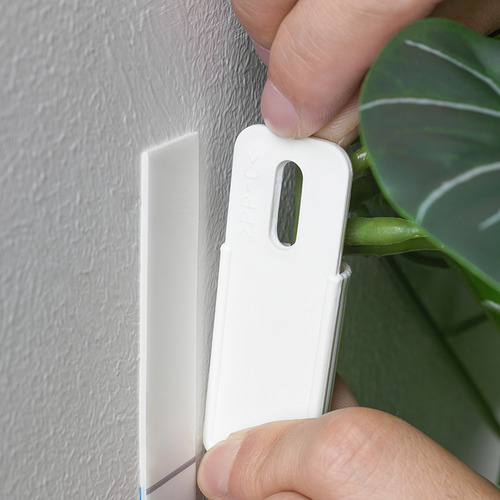 Una persona asegura una percha de plantas blancas en una pared, fijando una planta artificial en su lugar.