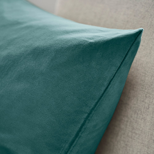 Primer plano de la lujosa funda de cojín de terciopelo verde azulado, suavemente drapeada, que resalta la textura afelpada y la fina artesanía.