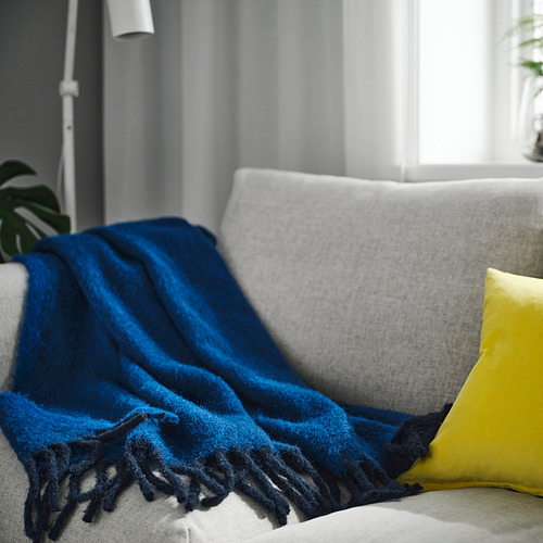 Manta azul KLIPPOXEL en sofá, grande, suave, con extremos con flecos, con almohada amarilla.