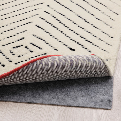 Una alfombra con patrones de diamantes tejidos y bordes rojos. Respaldo de fieltro para amortiguar el sonido y mayor comodidad.