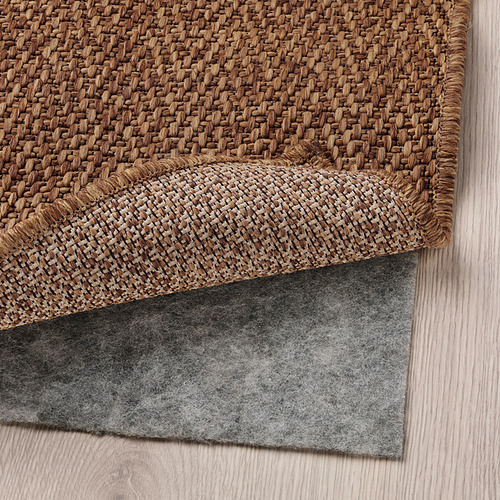 Una alfombra tejida con una alfombrilla antideslizante gris debajo, ideal para durabilidad y fácil cuidado, apta tanto para uso en interiores como en exteriores.