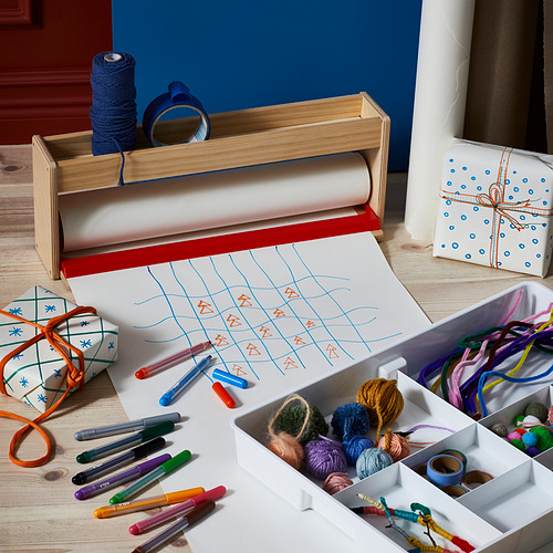 Estación de manualidades de madera con hilo de colores, rotuladores y papel de rollo para dibujar.
