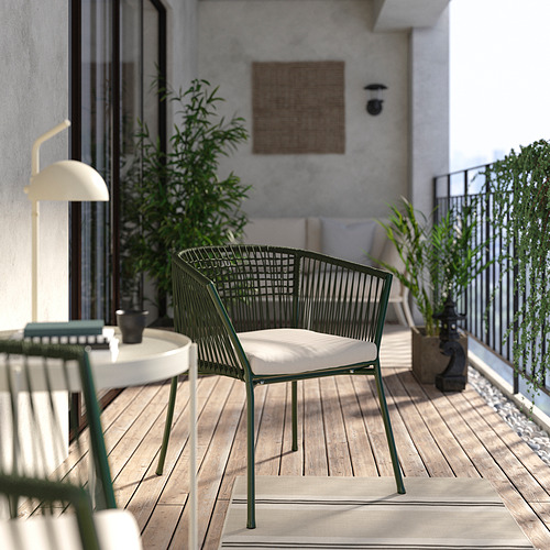 Escena de balcón con silla verde SEGERÖN, cojín blanco, lámpara, plantas y suelo de madera.